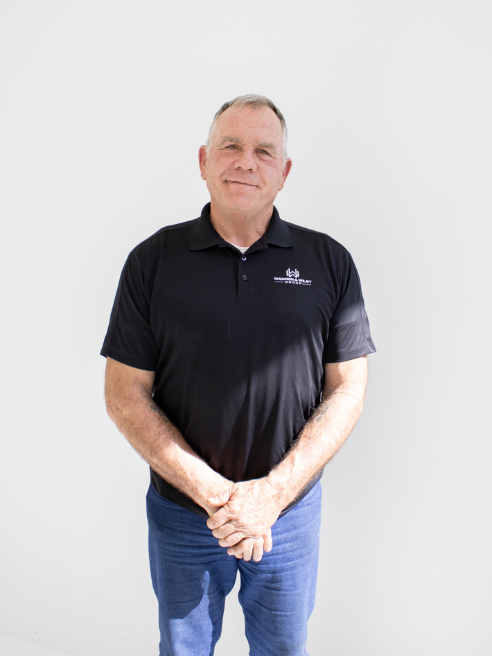 Man wearing a black polo shirt with a logo on a light gray background