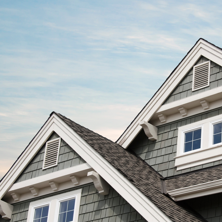 Roofline of a house with gray shingles and white trim against a blue sky.
